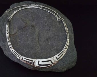 May include: A silver necklace with a geometric pattern. The necklace is made of a thick chain with a repeating pattern of interlocking squares.