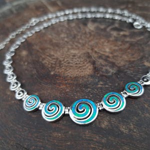 May include: A silver necklace with a chain made of small swirls. The necklace has five larger pendants, each with a blue and green opal swirl design.