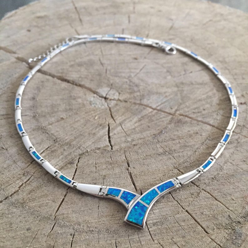 May include: A silver necklace with a V-shaped pendant set with blue opals. The necklace is made of small, linked silver pieces, each with a small blue opal inset.