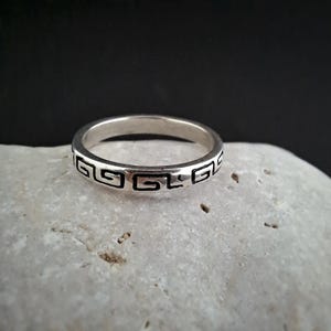 Könnte beinhalten: Ein Silberring mit einem geometrischen Muster um die gesamte Band.