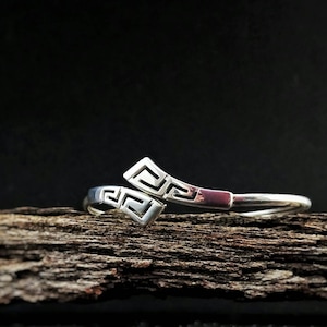 May include: Silver bracelet with a geometric design. The bracelet is on a piece of weathered wood.