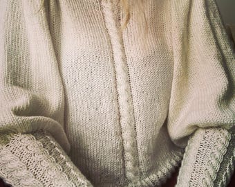 May include: Cream-colored knitted sweater with a high, ruffled collar and intricate cable detailing down the front. The sleeves are long with a textured pattern at the cuffs. The sweater has a relaxed fit with puffed sleeves.