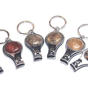 May include: Six silver nail clippers with keyrings. Each clipper has a different coloured and patterned round inlay. The inlays are brown, red, black, and white.