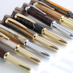 May include: A set of eight wooden pens with gold accents and silver tips. The pens are arranged in a row on a wooden stand.
