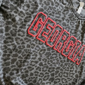 May include: A grey t-shirt with a leopard print pattern and the word "GEORGIA" in red outlined letters.