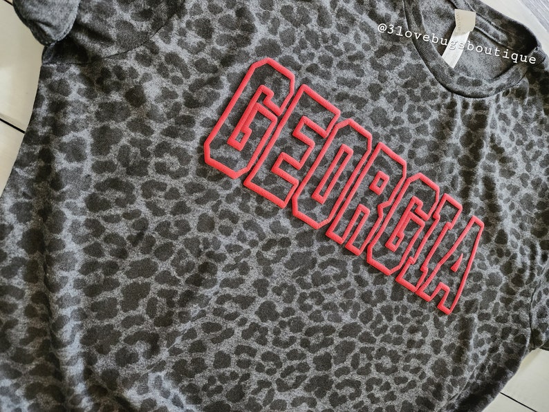 May include: A grey t-shirt with a leopard print pattern and the word "GEORGIA" in red outlined letters.