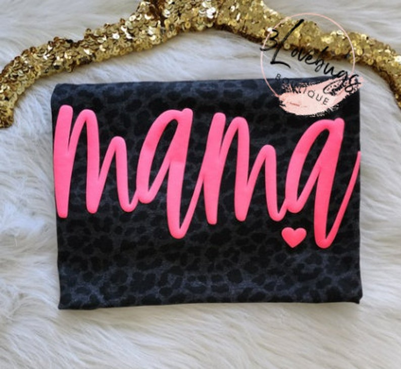 May include: Black and white leopard print t-shirt with the word "mama" in pink lettering and a small pink heart.