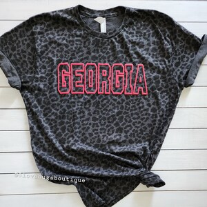 May include: A grey t-shirt with a black leopard print and the word "GEORGIA" in pink outlined letters.