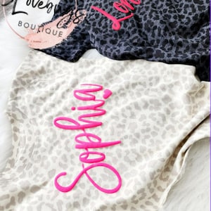 May include: Two leopard print shirts with pink lettering. One shirt says "London" and the other says "Sophia".