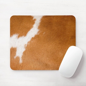 May include: A rectangular mousepad with a brown and white cowhide pattern. A white computer mouse is positioned on the right side of the mousepad. The mousepad has rounded corners and a textured surface.