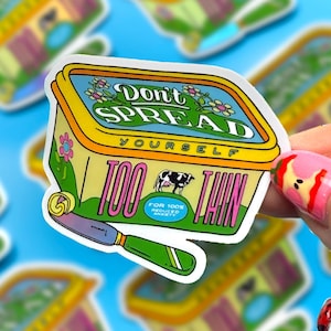 May include: A die-cut sticker featuring a yellow tub of spread with a green lid. The text reads Don't Spread Yourself Too Thin, with a small cow illustration and a butter knife with a curl of yellow butter on the blade. The design includes flowers.