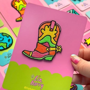Puede incluir: Un parche bordado colorido de una bota vaquera con un diseño de arcoíris. El parche está sobre un fondo rosa con el texto "by Liz harry @lizharrydesign".