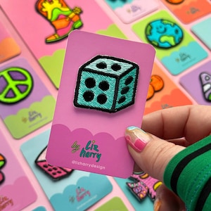 Könnte beinhalten: Ein gestickter Würfel-Patch in blaugrün mit schwarzen Punkten auf einer rosa Karte mit dem Text "by liz harry @lizharrydesign".