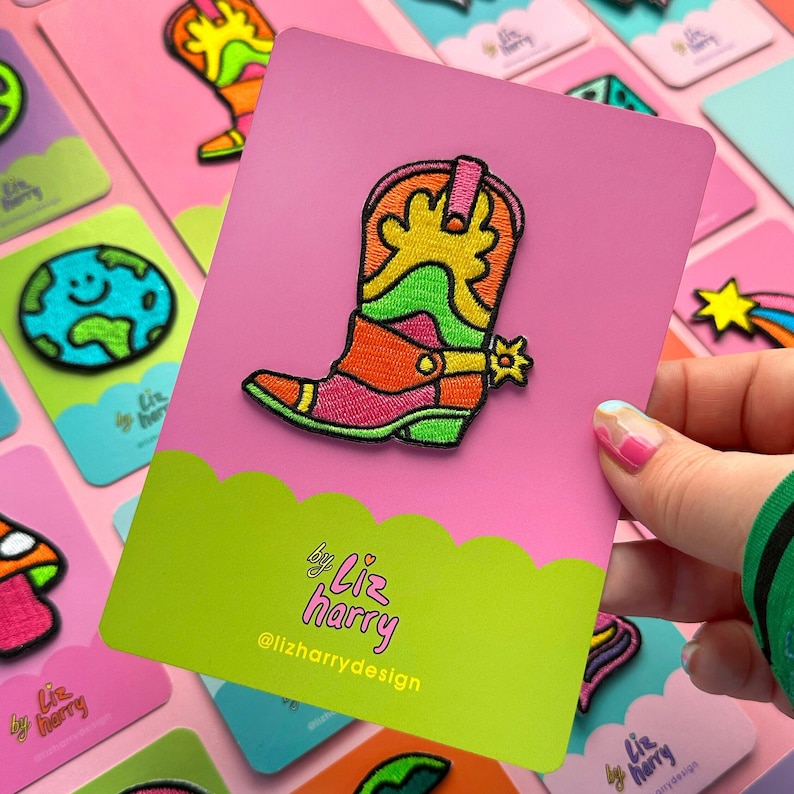 May include: A colorful embroidered patch of a cowboy boot with a rainbow design. The patch is on a pink background with the text "by Liz harry @lizharrydesign".