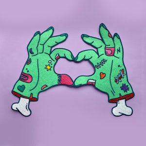 Peut inclure: Deux mains de zombie vertes avec divers détails colorés formant un cœur. Les mains sont cousues ensemble et ont une structure osseuse au niveau du poignet.