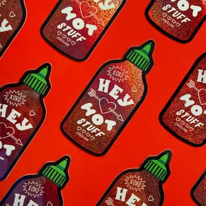 Op de afbeelding: Meerdere gestanste stickers in de vorm van hete sausflessen met een rode holografische afwerking. Elke sticker heeft een groene dop en witte tekst met HEY HOT STUFF, een hart doorboord door een pijl, het woord XOXO en 100% LOVE met vier hartjes.