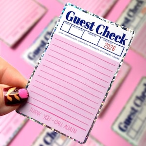 May include: A rectangular guest check notepad with a holographic glitter border. The top features the text Guest Check, table fields, and the number 2026. The centre has pink horizontal lines, and the bottom reads THANK YOU-CALL AGAIN.