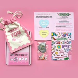 May include: Pink and white box with the text "Workshop in a Box" and a small pink bag with the text "Thank You" on it. The box contains a craft kit with instructions and a small bag of glitter.