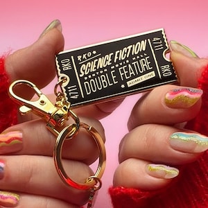 May include: Gold-coloured keychain with a black ticket-shaped charm that reads "RKO * SCIENCE FICTION DENTON MOVIE HALL DOUBLE FEATURE * ADMIT ONE RKO 4711 4711".