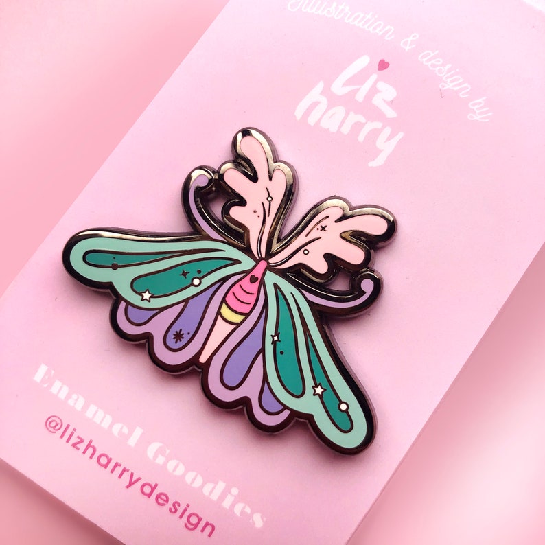 May include: A colorful enamel pin featuring a butterfly with pink, purple, green, and yellow wings. The butterfly has a silver outline and is decorated with small white stars. The pin is on a pink background with the text "Liz harry" and "Enamel Goodies @lizharrydesign".