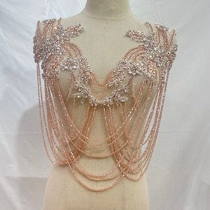 May include: A rose gold beaded and rhinestone embellished bridal or formal wear accessory. The piece features a delicate chain design with a large floral motif at the top.