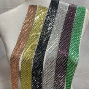 May include: Assortment of seven different colored rhinestone chain trims. The chains are made of small, square rhinestones in a variety of colors, including rose gold, gold, black, silver, purple, and green.