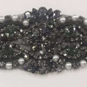 May include: A black and silver beaded trim with a central cluster of rhinestones. The trim is approximately 1.5 inches wide and is perfect for adding a touch of sparkle to any project.