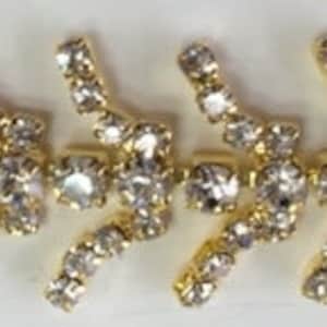 May include: A gold chain with clear rhinestones arranged in a repeating pattern of a curved arrow shape.