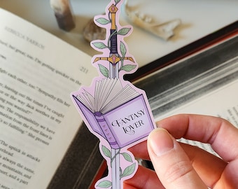 Op de afbeelding: Een roze sticker met een zwaard en een boek. Het boek is paars en heeft de tekst "Fantasy Lover" op de kaft. Het zwaard is omgeven door groene wijnstokken.