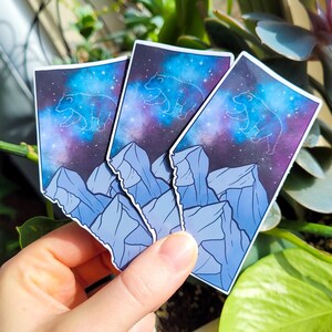 May include: Three stickers featuring a constellation bear design with a blue, purple, and black galaxy background. The bear is outlined in white and the mountains are a light blue colour.