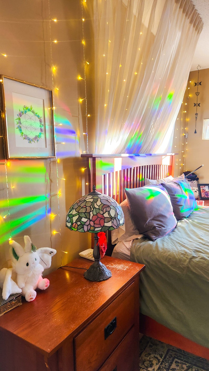 May include: A bedroom with a bed, a nightstand, a lamp, and a stuffed animal. The bed has a white canopy and a green duvet. The nightstand is made of wood and has a drawer. The lamp is a stained glass lamp with a floral design. The stuffed animal is a white bunny with wings.