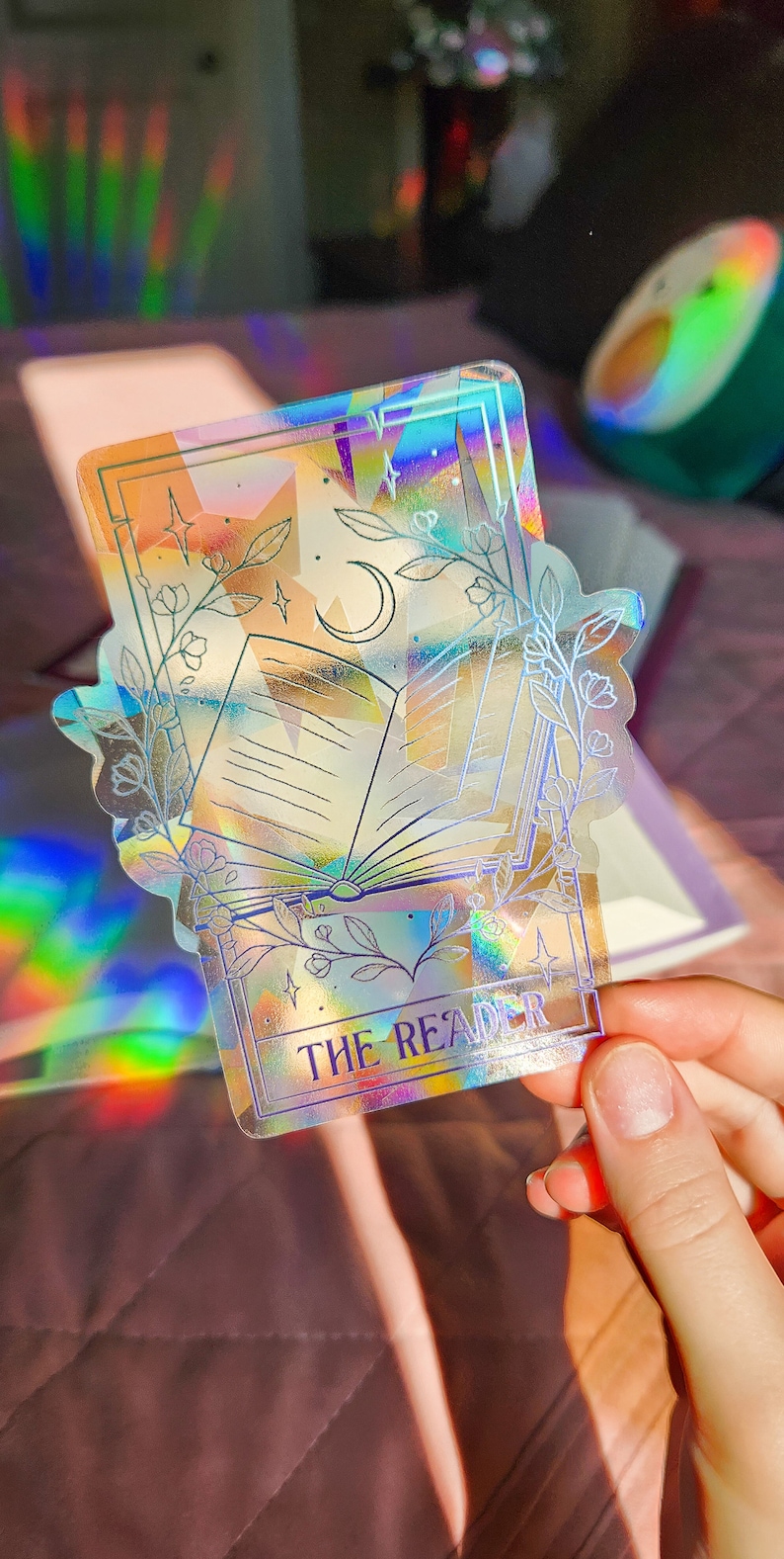 May include: A holographic sticker with a book, moon, and stars. The sticker has a white border and the text "THE READER" at the bottom.