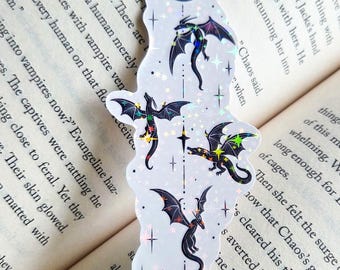 Pode incluir: Um autocolante holográfico vertical com uma lua crescente no topo e na base, ligadas por uma linha fina com quatro pequenos dragões pretos em voo. O design inclui estrelas e brilhos holográficos dispersos num fundo branco.