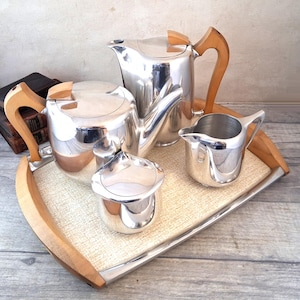 May include: A polished silver tea set comprising a teapot, milk jug, sugar bowl, and serving tray. The set features wooden handles and accents. The tray has a light-colored surface with a wooden frame, offering a classic and elegant appearance.