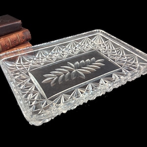 May include: A rectangular clear glass tray featuring a faceted diamond-cut pattern along the raised edges and a central frosted glass panel decorated with an etched leaf motif. The tray has a thick, transparent rim and a smooth, flat base.