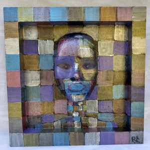 May include: A wooden framed artwork with a mosaic-style portrait of a person. The portrait is made up of small squares of different colors, including purple, blue, green, and gold. The artwork is signed "RK" in the lower right corner.