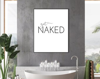 May include: A modern bathroom scene featuring a white, oval bathtub and a framed print with the words "get NAKED" in black. A wooden side table holds toiletries, and a large potted plant adds greenery. The room has a minimalist design with a view of nature.