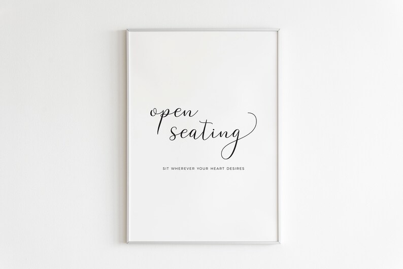 May include: A framed print with the words "open seating" in elegant script. Below, the text reads "Sit wherever your heart desires." The artwork is in black and white, with a minimalist design.