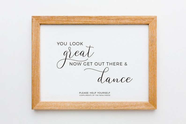 May include: A framed print with a light wood grain frame. The white background features elegant black script that reads "YOU LOOK great NOW GET OUT THERE & dance." Below, smaller text says "PLEASE HELP YOURSELF COMPLIMENTS OF THE NEWLYWEDS."