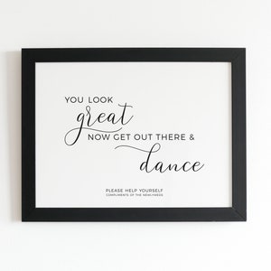 May include: A framed print with a black border. The white background features elegant black script that reads "YOU LOOK great NOW GET OUT THERE & dance." Below, smaller text says "PLEASE HELP YOURSELF COMPLIMENTS OF THE NEWLYWEDS."