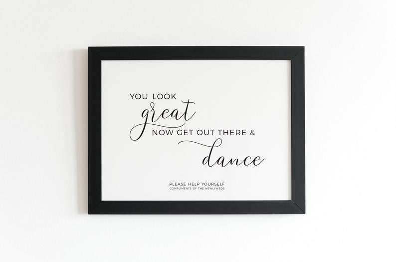 May include: A framed print with a black border. The white background features elegant black script that reads "YOU LOOK great NOW GET OUT THERE & dance." Below, smaller text says "PLEASE HELP YOURSELF COMPLIMENTS OF THE NEWLYWEDS."