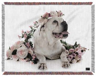May include: White boxer dog wearing a flower crown and surrounded by pink and white roses. The dog is lying down on a white background. The image is a woven tapestry.