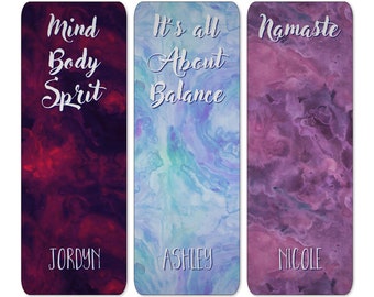 May include: Three yoga mats with watercolor designs. The first mat is red and purple with the text "Mind Body Sprit" and the name "JORDYN". The second mat is blue and green with the text "It's all About Balance" and the name "ASHLEY". The third mat is purple with the text "Namaste" and the name "NICOLE".
