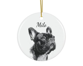 May include: A round, white ceramic ornament with a pencil sketch of a French Bulldog. The dog is black and white, with the name "Milo" in cursive script above the dog's head. A gold string is attached for hanging.