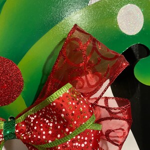 K&ouml;nnte beinhalten: Eine rot-gr&uuml;ne Weihnachts Schleife mit wei&szlig;en Punkten und Glitzer. Die Schleife ist aus durchsichtigem Stoff und hat ein gr&uuml;nes Band, das darum gebunden ist.