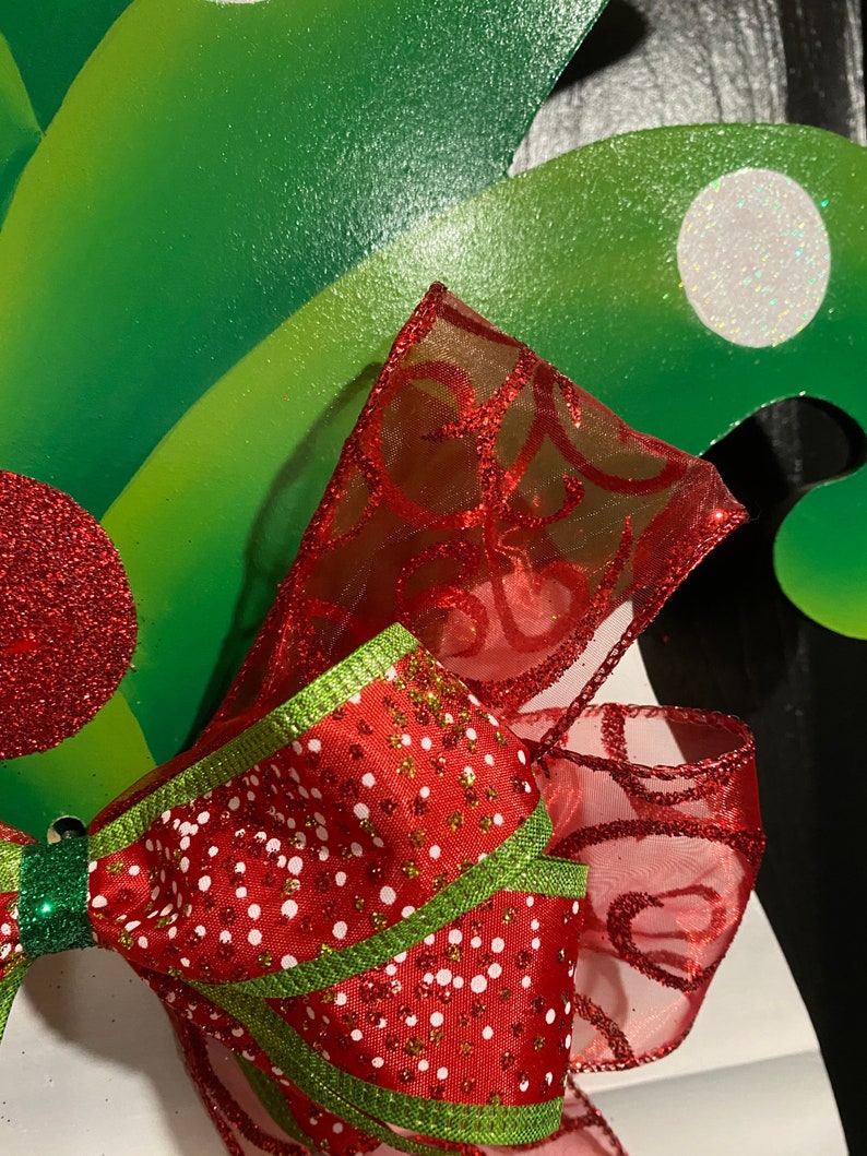 K&ouml;nnte beinhalten: Eine rot-gr&uuml;ne Weihnachts Schleife mit wei&szlig;en Punkten und Glitzer. Die Schleife ist aus durchsichtigem Stoff und hat ein gr&uuml;nes Band, das darum gebunden ist.