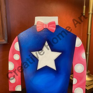 Puede incluir: Recorte decorativo de madera de sedas de jockey. Las sedas son azules con una estrella blanca, mangas rosas con lunares blancos y una pajarita rosa. El recorte est&aacute; dise&ntilde;ado para estar de pie.