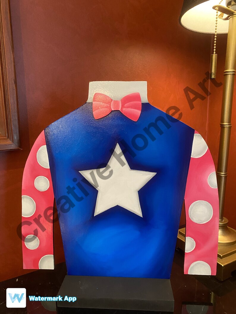 Puede incluir: Recorte decorativo de madera de sedas de jockey. Las sedas son azules con una estrella blanca, mangas rosas con lunares blancos y una pajarita rosa. El recorte est&aacute; dise&ntilde;ado para estar de pie.