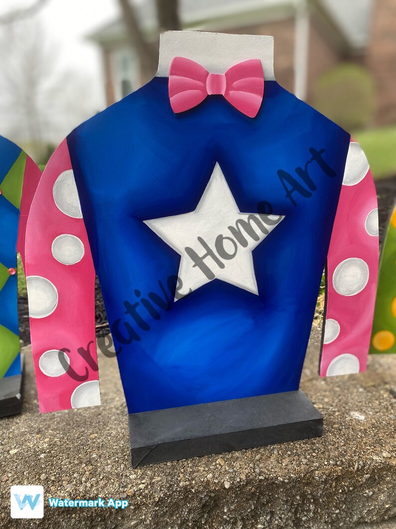 Puede incluir: Recorte de madera de la casaca de un jockey. La casaca es azul con una estrella blanca, mangas rosas con lunares blancos y una pajarita rosa. El texto "Creative Home Art" es visible.