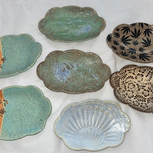 May include: Six ceramic dishes with various patterns and colors. The dishes are oval shaped and have a raised edge. The patterns include floral, geometric, and abstract designs. The colors include green, brown, gold, and white.
